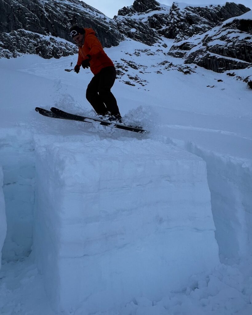Eine Person springt mit Skiern auf einen freigestellten Rutschblock.