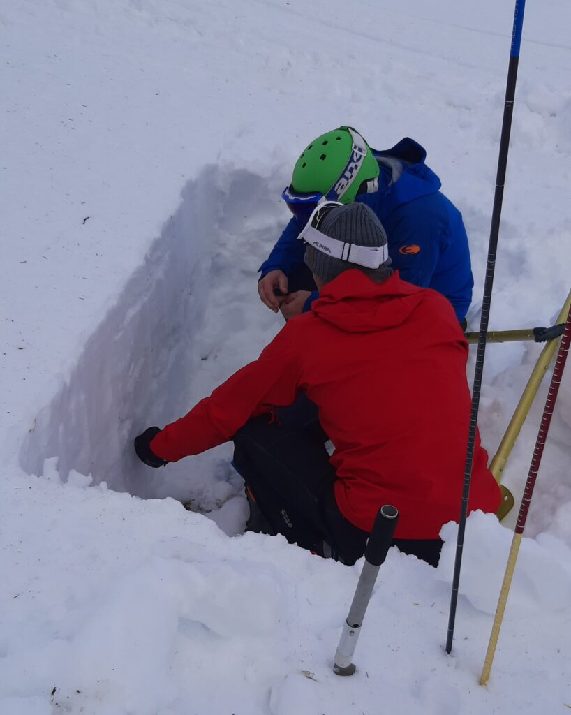 Zwei Lehrgangsteilnehmer des Aufbaulehrgangs bei der Schneedeckenuntersuchung vor einem Profil.